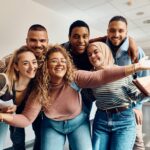 Group of cheerful college students having fun in a hallway and looking at camera.