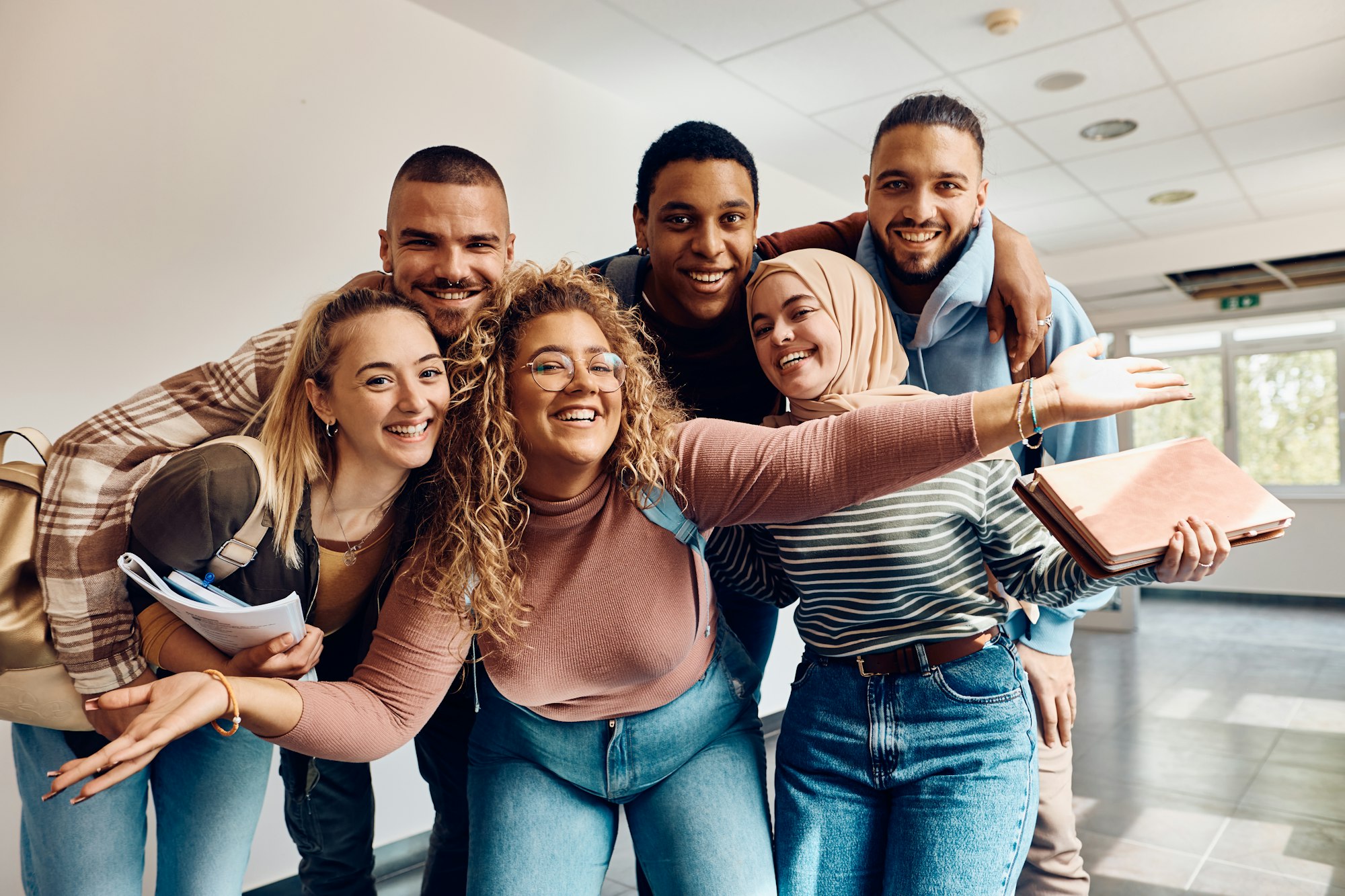 Group of cheerful college students having fun in a hallway and looking at camera.