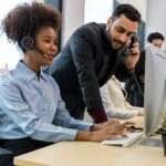 Call center business woman talking on headset. Call center worker accompanied by her team.